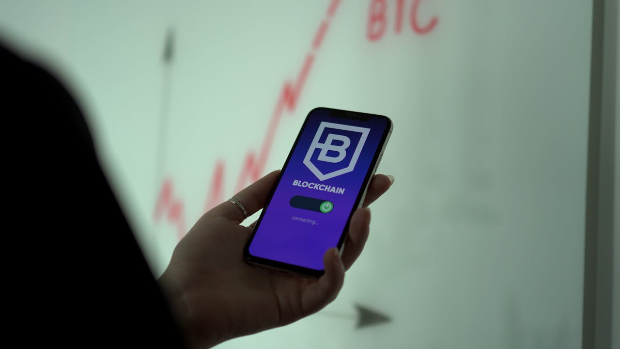 A close-up of a hand holding a smartphone displaying a blockchain app with a stock graph in the background.