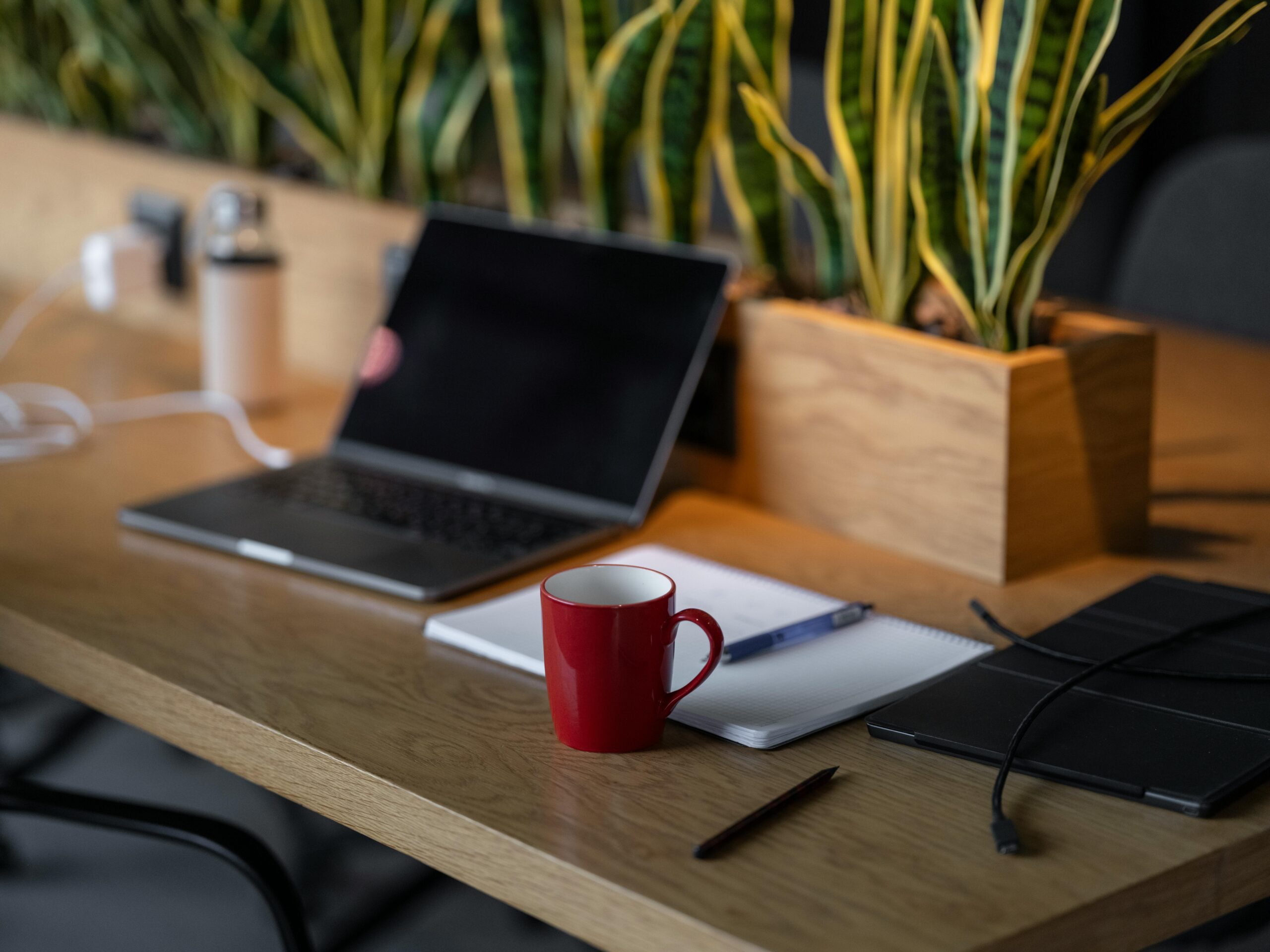 Laptop open on a wood desk beside a red coffee mug and open notebook, ready for tax and bookkeeping work